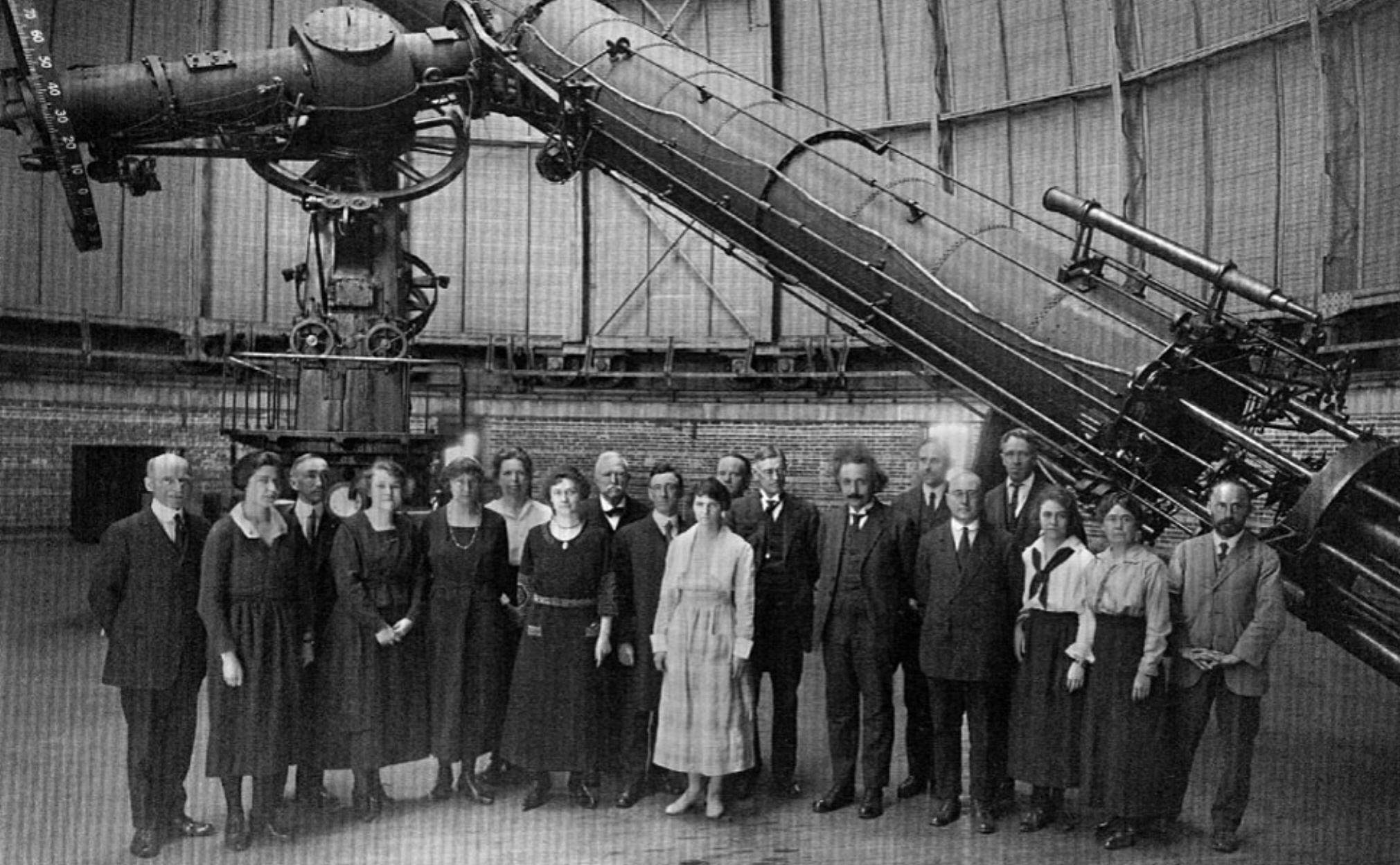 A group of individuals, including Albert Einstein, who is just to the right of center, standing for a formal portrait in front of the Yerkes Telescope, within the dome.